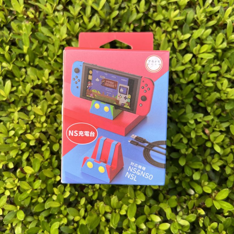 Empaque de la base de carga portátil Mario Bros para Nintendo Switch con puerto Tipo C sobre un fondo de plantas verdes.